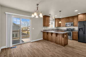 Kitchen featuring wood cabinetry, stainless steel appliances, a peninsula, hanging lights, and new flooring