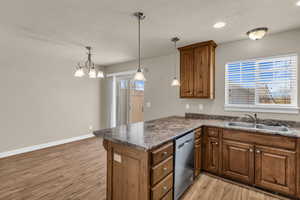 Kitchen with a peninsula, wood finish cabinetry, dark countertops, light wood-style flooring, and dishwasher