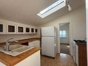 Kitchen with white cabinets, white appliances, parquet flooring, a skylight, and lofted ceiling