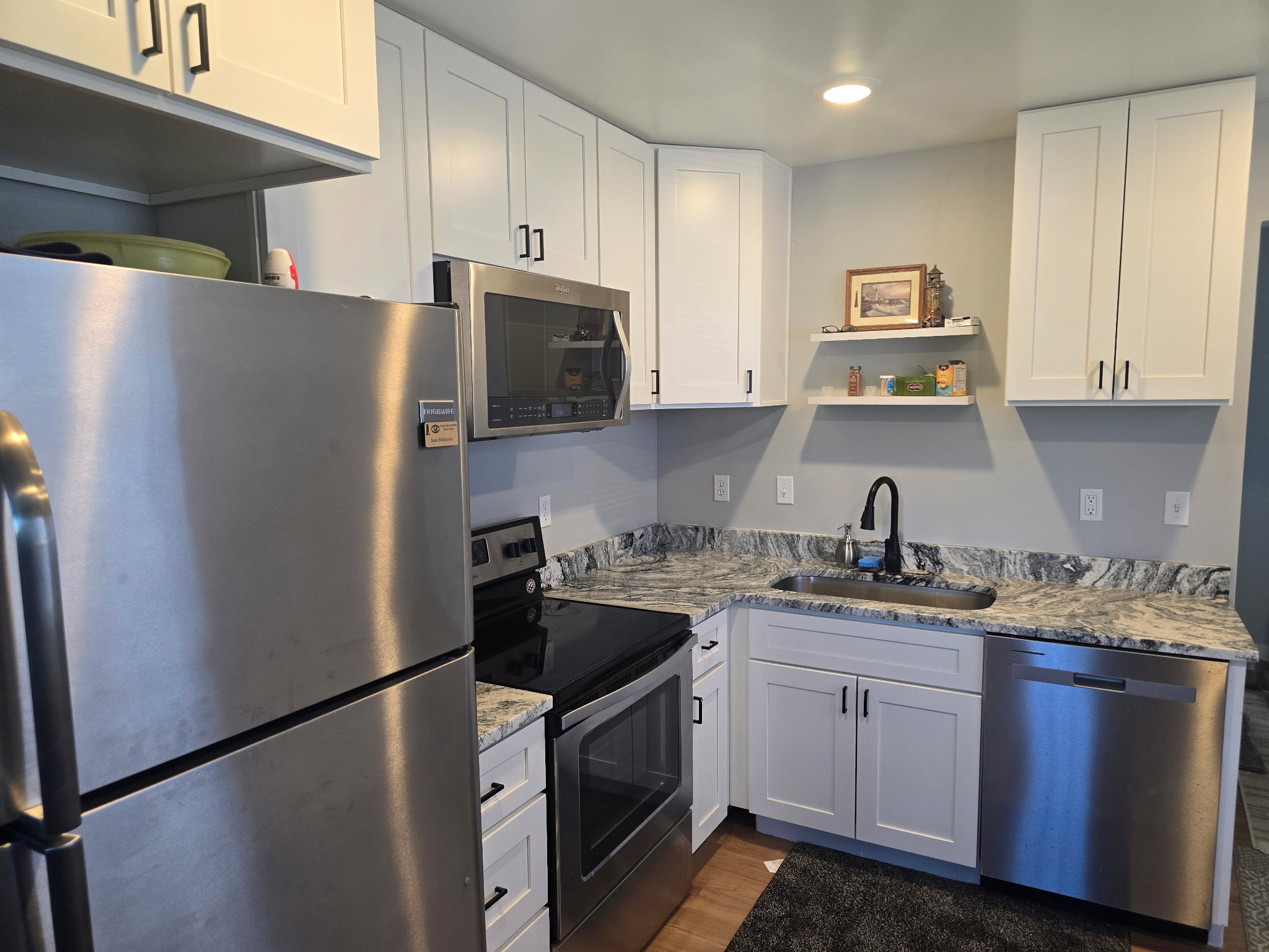 Kitchen with stainless steel appliances, white cabinets, light stone counters, open shelves, and recessed lighting