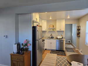 Kitchen featuring white cabinets, stainless steel appliances, light wood finished floors, open shelves, and light stone countertops