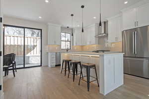 Kitchen featuring stainless steel appliances, a breakfast bar, white cabinetry, a kitchen island, and light wood finished floors