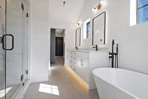 Full bath featuring double vanity, light tile patterned floors, a marble finish shower, vaulted ceiling, and a freestanding tub