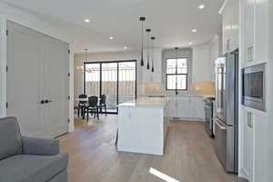 Kitchen with white cabinets, stainless steel appliances, light wood-style floors, a center island, and light stone counters