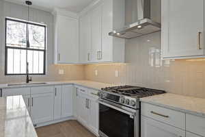 Kitchen with stainless steel gas range, white cabinets, light stone counters, and wood finished floors
