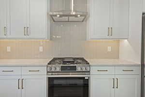 Kitchen with stainless steel range with gas cooktop, white cabinetry, light stone countertops, and backsplash