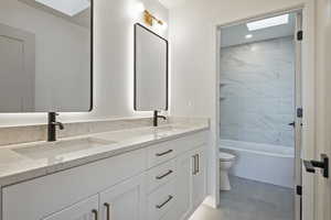 Bathroom featuring a skylight, double vanity, and shower / bathtub combination