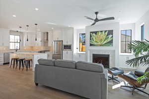 Living area with light wood-type flooring, a high end fireplace, ceiling fan, and recessed lighting