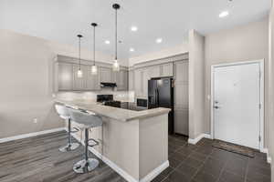 Kitchen featuring a breakfast bar, a peninsula, black appliances, gray cabinetry, and pendant lighting