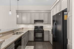 Kitchen with black appliances, light stone counters, gray cabinetry, and decorative light fixtures