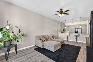 Living room with light wood-style floors, ceiling fan, and recessed lighting