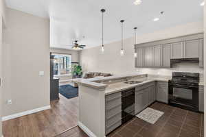 Kitchen featuring black appliances, gray cabinets, a peninsula, hanging light fixtures, and light stone countertops