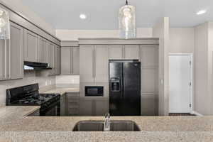 Kitchen featuring black appliances, gray cabinetry, pendant lighting, and light stone counters