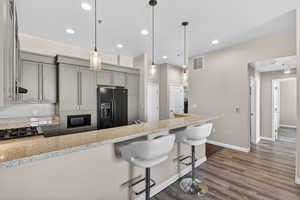 Kitchen featuring black appliances, dark wood-style floors, light stone counters, a kitchen bar, and decorative light fixtures