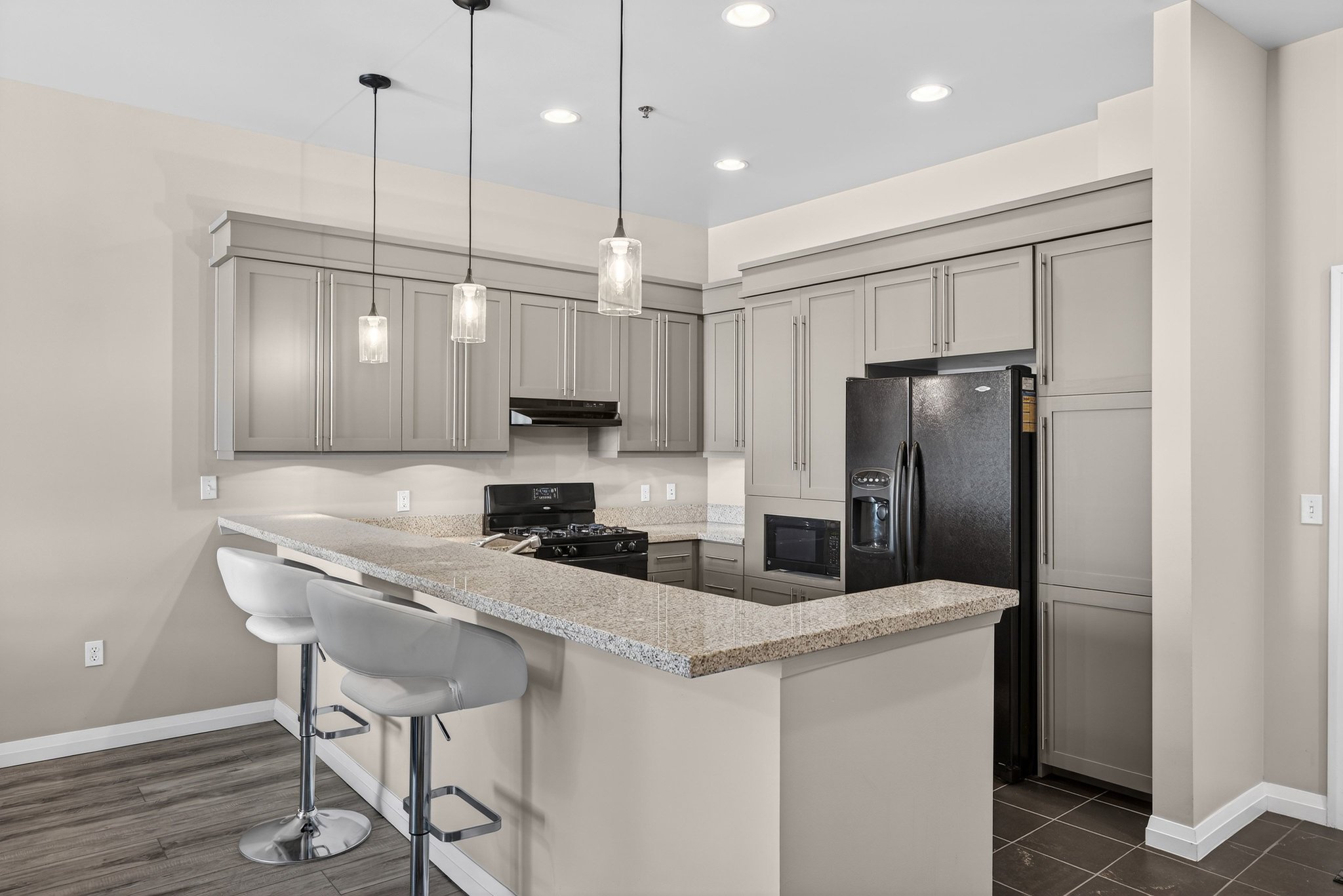 Kitchen with black appliances, hanging light fixtures, a peninsula, a breakfast bar area, and light stone countertops