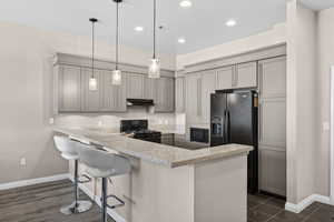 Kitchen with black appliances, hanging light fixtures, a peninsula, a breakfast bar area, and light stone countertops