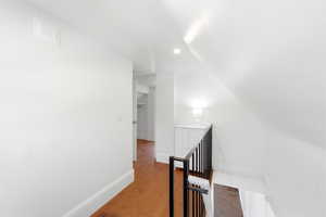 Hall with an upstairs landing, wood finished floors, vaulted ceiling, and recessed lighting
