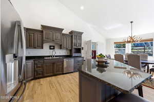 Kitchen featuring stainless steel appliances, dark wood finish cabinetry, dark stone countertops, vaulted ceiling, and a chandelier