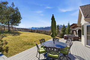 Wooden deck featuring a hot tub, outdoor dining area, a fenced backyard, and a mountain view