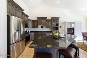 Kitchen with stainless steel appliances, dark wood finish cabinets, dark stone countertops, independent washer and dryer, and lofted ceiling