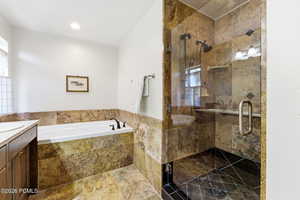 Full bath with vanity, a garden tub, a stall shower, and dark stone finish floors