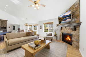 Living room with lofted ceiling, light wood-type flooring, a ceiling fan, a fireplace, and suspended lighting