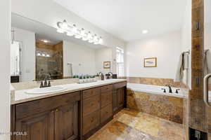 Bathroom featuring a stall shower, double vanity, stone tile floors, and a garden tub
