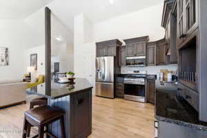 Kitchen with dark stone countertops, open floor plan, stainless steel appliances, a center island, and dark wood finish cabinetry