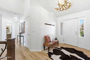 Entrance foyer with light wood-type flooring, a chandelier, and vaulted ceiling