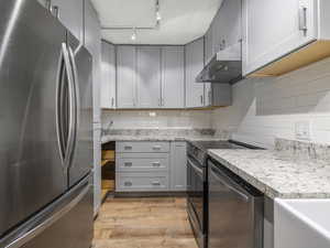 Kitchen featuring gray cabinets, stainless steel appliances, light stone counters, tasteful backsplash, and light wood-type flooring