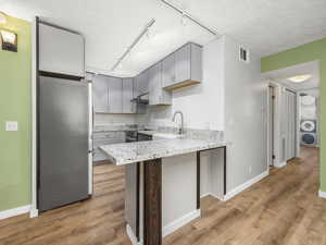 Kitchen with stainless steel appliances, rail lighting, a peninsula, gray cabinetry, and light wood-type flooring