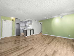 Unfurnished living room with rail lighting, light wood-style flooring, and a textured ceiling