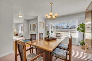Dining area featuring light carpet, a textured ceiling, suspended lighting, and plenty of natural light