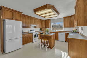 Kitchen featuring wood finish cabinetry, light flooring, white appliances, a kitchen breakfast bar, and light countertops