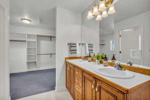 Bathroom featuring double vanity, a spacious closet, light carpet, and a textured ceiling