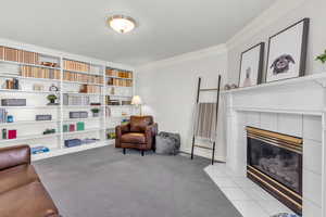 Sitting room with ornamental molding, light colored carpet, a textured ceiling, a tiled fireplace, and built in shelves