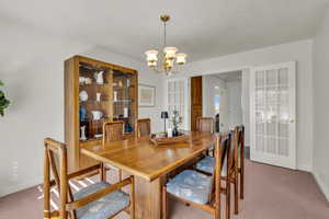 Dining area featuring light carpet, a chandelier, and a textured ceiling