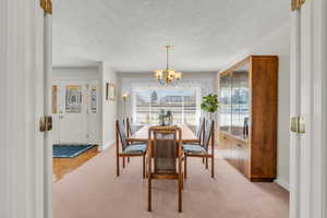 Dining space with a chandelier, a textured ceiling, and light carpet