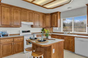 Kitchen featuring white appliances, wood finish cabinetry, light floors, a kitchen breakfast bar, and a center island