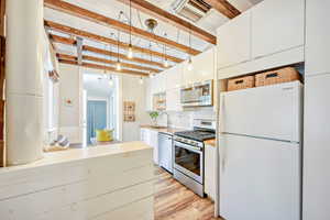 Kitchen with stainless steel appliances, beam ceiling, light countertops, decorative backsplash, and light wood finished floors