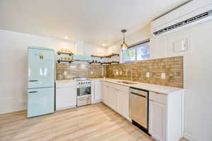 Kitchen featuring stainless steel appliances, white cabinets, light wood finished floors, hanging light fixtures, and open shelves
