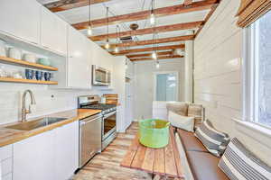 Kitchen featuring open shelves, stainless steel appliances, white cabinets, light wood-style flooring, and beam ceiling