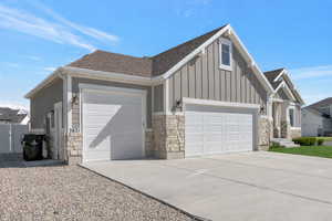 View of front of house featuring stone siding, an attached garage, driveway, board and batten siding, and a shingled roof