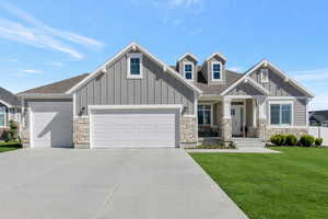 Craftsman-style house featuring board and batten siding, stone siding, a front yard, and an attached garage