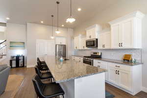 Kitchen featuring a kitchen bar, stainless steel appliances, white cabinetry, and dark wood-type flooring