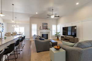Living room featuring dark wood-style flooring, lofted ceiling, hanging lights, a ceiling fan, and plenty of natural light