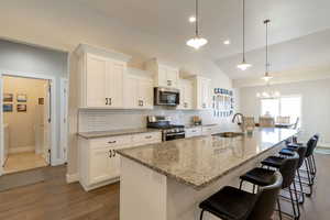 Kitchen with light stone countertops, a kitchen breakfast bar, stainless steel appliances, an island with sink, and white cabinets