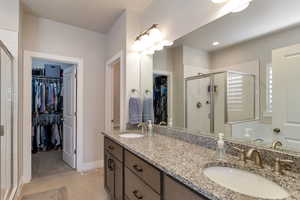 Bathroom featuring a walk in closet, a shower stall, double vanity, and light tile patterned floors