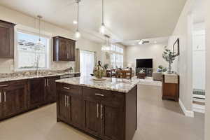 Kitchen with open floor plan, a center island, light stone counters, dark wood finish cabinets, and ceiling fan