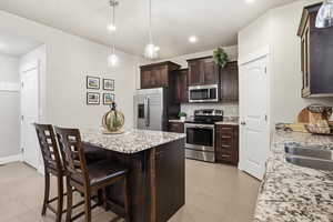 Kitchen with stainless steel appliances, dark wood finish cabinets, light stone countertops, a kitchen breakfast bar, and a center island